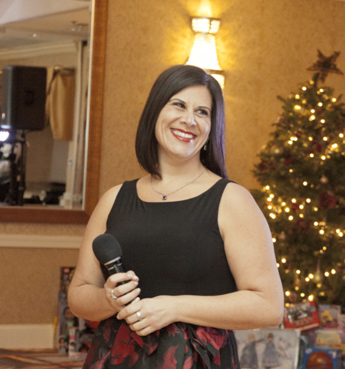 Nicole Comis speaking confidently on stage at the DuPage County Toys for Tots Gala, a charity event she hosted.